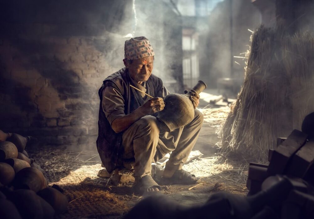 The old man is painting in a clay pot in Durbar square near old hindu temples.