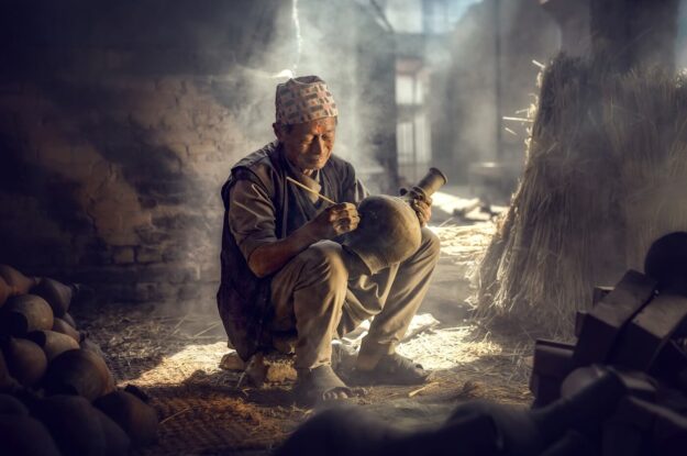 The old man is painting in a clay pot in Durbar square near old hindu temples.