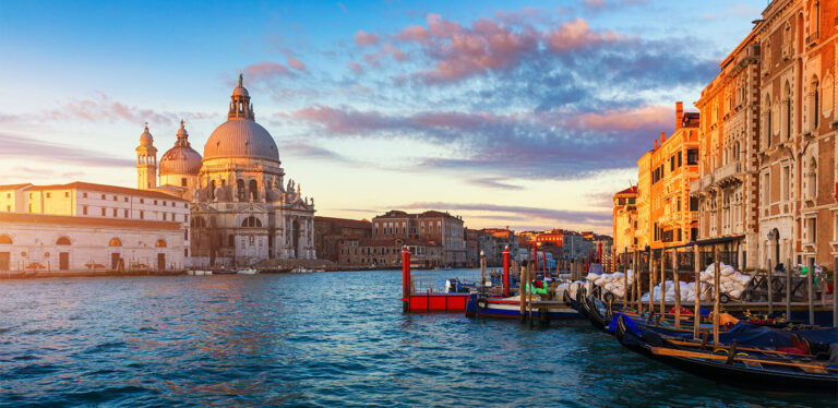 “Panoramic sunset view of Venice’s Grand Canal with historic architecture and moored gondolas, capturing the essence of Italian travel.”