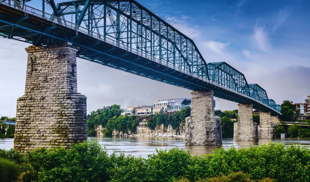 a bridge spanning over a river with trees and buildings in the background