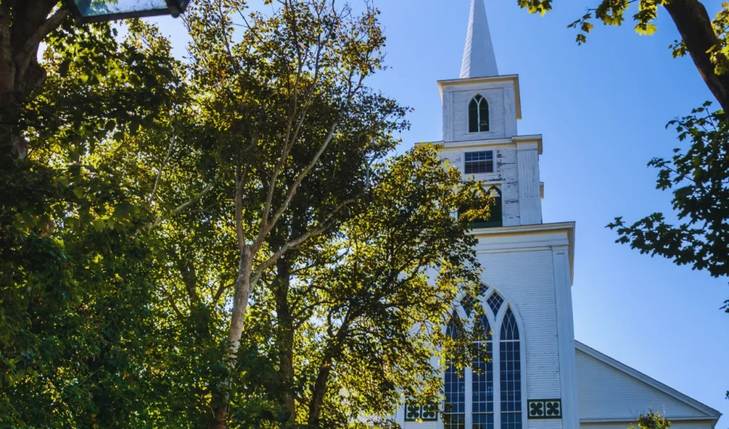 a church with a steeple in the middle of a wooded area